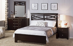 photo of black wooden bed frame with mattress, bed sheet, and pillows between nightstand and dresser with mirror